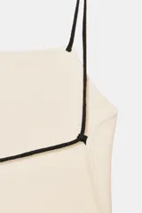 Top de punto color crema, de escote recto y corte holgado, con tirantes finos negros que se cruzan en la espalda.