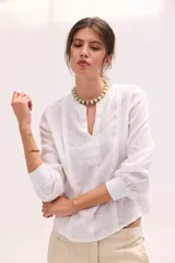Blusa blanca de lino con escote en V y mangas largas con puños elásticos, combinando delantera estructurada de lino y espalda de algodón con spandex.