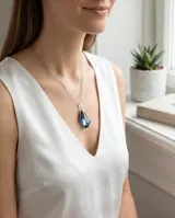 Collar de plata con cadena fina y dije de cristal facetado en forma de gota con tonalidades azul y violeta.
