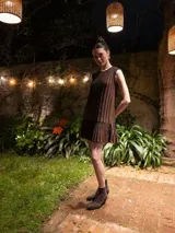 Vestido corto sin mangas, de corte recto con volado en el ruedo. Presenta un diseño de rayas verticales en tonos marrón y negro con sutiles hilos de lurex brillantes.