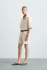 Bermuda de algodón color blanco, de corte relajado, con cintura elástica, bolsillos frontales y bolsillos traseros de plastrón. Cierre frontal con cremallera y botón.