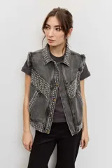 Campera de jean color gris con efecto acid wash, corte clásico y cierre frontal de botones metálicos. Presenta cuello camisero, bolsillos ribeteados y está decorada con apliques de tachas plateadas en el cuello, el canesú frontal, los bordes de la botonera, los bolsillos y el ruedo.