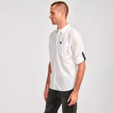 Camisa blanca de popelina con mangas largas enrollables con trabilla, bolsillo en el pecho con logo de la marca y dobladillo camisero.