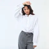 Camisa de popelina blanca con cuello clásico, cierre frontal de botones y mangas largas abullonadas con puños ajustados.