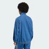 Chaqueta deportiva Adidas Firebird Adilenium de denim, color azul, con cuello alto, cierre frontal y las clásicas tres tiras en las mangas. Cuenta con bolsillos frontales ribeteados y el logo del trifolio bordado en el pecho.