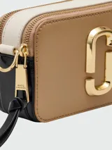 Cartera crossbody Marc Jacobs modelo The Snapshot, color tostado con herrajes dorados y logo frontal metálico. Incluye correa ajustable y extraíble con diseño de marca estampado.