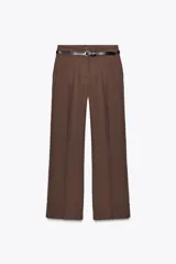 Pantalón de vestir marrón oscuro, tiro alto, corte ancho y pierna recta. Presenta pinzas frontales, puños anchos doblados (vuelta) y se complementa con un cinturón fino negro con hebilla metálica dorada.