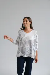 Sweter de punto con escote en V y mangas largas, de corte holgado. Presenta un estampado abstracto en tonos grises y blancos con sutiles destellos brillantes.