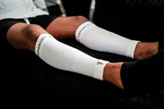 Medias de compresión blancas de caña alta, diseñadas para brindar soporte y mejorar la circulación durante la actividad física. Presentan un tejido técnico acanalado con el logo de la marca estampado en la parte superior y un pequeño detalle bordado en el borde inferior.