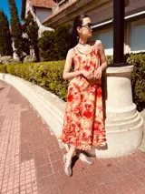 Vestido largo de lino con estampado tie-dye en tonos naranja, rojo y amarillo. Tiene breteles finos y volados en el ruedo.