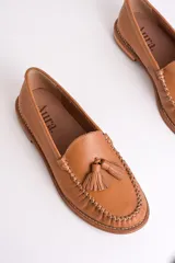 Mocasines negros de cuero con borlas y costuras decorativas.