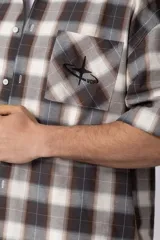 Camisa de manga corta de popelina cuadrillé en tonos marrón, blanco y gris, con diseño boxy fit, cuello camisero, cierre frontal de botones, bolsillo en el pecho con detalle bordado y dobladillo recto.