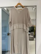 Vestido midi beige de corte holgado, compuesto por una capa superior de tejido de red transparente con mangas cortas y detalles deshilachados, sobre una base de tela lisa.