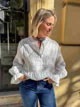 Blusa blanca de manga larga con detalles de bordado floral y calados en el frente. Presenta cuello mao con cierre frontal de botones y puños con volados.