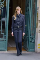 Blusa de denim en color azul oscuro con cuello inglés, cierre frontal con botones y tiras integradas en el cuello para anudar. Presenta mangas largas con puños anchos abotonados y costuras reforzadas.