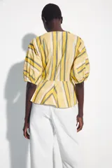 Camisa de algodón con rayas amarillas, blancas y grises, cuello redondo, mangas cortas abullonadas con puños elásticos y bajo con vuelo evasé.
