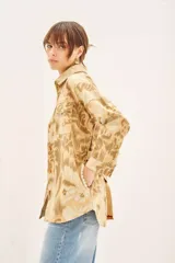 Campera de corte recto confeccionada en gabardina de algodón, con diseño estampado y detalles bordados. Presenta cuello camisero, cierre frontal con botones, bolsillos con solapa en el pecho y lazo ajustable en la cintura con terminaciones bordadas.