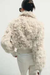 Chaqueta tipo bomber de textura afelpada en color crema, con cuello solapa, cierre frontal con cremallera y puños y cintura de tejido elástico acanalado.
