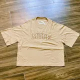 Remera color arena con cuello redondo y estampado frontal con letras "MTPE" en marrón.