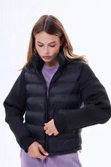 Campera negra de estilo híbrido, con cuerpo acolchado y mangas de tejido liso. Presenta cuello alto, cierre frontal y puños elásticos.