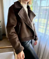 Campera de gamulán color marrón chocolate, con interior y detalles en corderito al tono. Presenta cierre frontal cruzado, cuello solapa amplio y bolsillos laterales con cierre metálico.