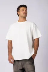 Remera de corte oversized en color marrón, confeccionada en tejido de algodón con textura de micropanal. Presenta cuello redondo con detalle de costura en forma de X y mangas cortas de estilo caído.