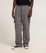 Pantalón convertible de estilo cargo color gris, con cintura elástica y cordón de ajuste. Presenta bolsillos laterales y diseño funcional que permite convertirlo en bermuda mediante cierres en la zona de los muslos. Incluye tiradores en los tobillos para ajustar el ruedo.