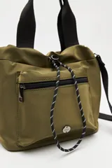 Cartera tipo bolso de nylon negro, con diseño utilitario y formato flexible que se ajusta con cordón en la parte superior. Posee asas de mano y una correa ajustable y desmontable para llevar cruzada. Incluye bolsillo frontal con cierre y herrajes metálicos.
