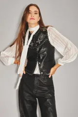 Chaleco de cuero ovino negro con diseño sin mangas, cierre frontal con botones metálicos y detalles de tachas plateadas formando patrones de estrellas en la parte superior delantera.