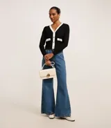 Cardigan de punto blanco con escote en V, botones metalizados, bolsillos falsos, cuello y vista contrastantes en negro, y bajo acanalado.