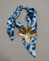Pañuelo de seda celeste con estampado animal print azul y un dije metálico dorado en forma de flor que sujeta la prenda.