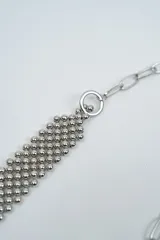 Cinturón de cadena plateada con diseño de malla central de esferas pequeñas y terminaciones con dijes en forma de corazón.