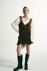 Vestido corto color marrón con escote en pico y tirantes anchos. Presenta un diseño con múltiples volantes en cascada que recorren el frente y el bajo, con un acabado asimétrico.