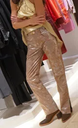 Pantalón de cuero color marrón con estampado abstracto, corte acampanado y abertura en el ruedo.