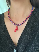Collar corto con cuentas alternadas de cerámica roja y cuentas azules oscuras, con un dije colgante de coral rojo esmaltado.