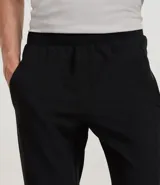 Pantalón deportivo masculino de microfibra color negro, corte recto, con cintura elástica y bolsillos con cremallera. Confeccionado en poliéster y elastano.