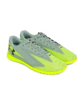 Championes de fútbol Under Armour Shadow Select 3 Turf, diseñados para césped artificial. Presentan un empeine sintético suave y resistente en color gris con detalles en amarillo neón, incluyendo el logo de la marca en negro. Cuentan con suela de goma con tacos multidireccionales para un agarre óptimo.