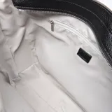 Cartera tipo tote bag color negro, con textura símil cuero y logo 'XL' en el frente. Tiene doble asa de mano y cierre superior. El interior está forrado en tela y cuenta con un bolsillo con cierre.