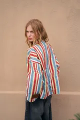 Camisa de denim azul con cuello mao, diseño holgado, mangas largas y cierre frontal con botones metálicos. Cuenta con costuras decorativas pespunteadas en el delantero.