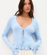 Saco de tricot celeste con textura acanalada vertical, escote en V y cierre frontal con lazos atables. Presenta mangas largas con puños acampanados con volados, al igual que el ruedo.