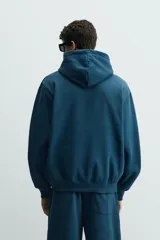 Sudadera con capucha de corte relajado, confeccionada en tejido de algodón con interior perchado. Presenta mangas largas, bolsillo frontal tipo canguro y terminaciones en rib.