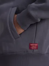 Canguro con cierre frontal completo, confeccionado en tejido fleece de color azul marino. Presenta capucha con cordones ajustables, bolsillos laterales y puños y ruedo acanalados.