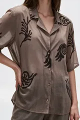 Camisa de algodón con estampado en tonos claros sobre base azul oscura, cuello solapa, mangas cortas y cierre frontal con botones.
