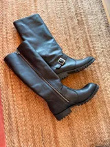 Botas de cuero negro de caña alta con cierre lateral y hebilla decorativa.