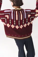 Campera tipo bomber tejida con diseño jacquard geométrico en tonos azul marino, blanco, rojo y verde. Presenta cierre frontal completo, cuello, puños y ruedo acanalados en color verde y blanco, con corte oversized y hombros caídos.