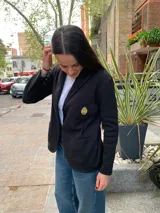 Blazer negro de tejido de punto en algodón, con solapas, dos bolsillos frontales y un escudo bordado en el pecho. Corte recto y holgado.
