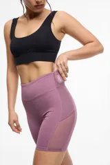 Short deportivo tipo biker de cintura alta, color violeta, con paneles laterales de microtul y bolsillos integrados.