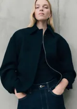 Chaqueta oversize de tejido mezcla de lana en color negro, con cuello camisero, cierre frontal de cremallera oculta, bolsillos laterales y mangas largas con puños abotonados.