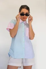 Camisa de manga corta con diseño de rayas en tonos rosa, celeste, verde y blanco. Cuenta con cuello camisero, cierre frontal con botones y un bolsillo en el pecho.