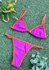 Bikini de dos piezas color fucsia con bordes en naranja. El corpiño es triangular con tirantes finos y la bombacha es colaless regulable con tiras finas laterales.